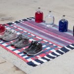Amanda Ross-Ho and Diedrick Brackens. <em>Untitled Floor Arrangement (300 bucks would save my life)</em>, 2017. Handwoven cotton rugs, glass jugs, Procion dyes, Nike Dunks, and Reebok Pumps, 12 1/4 x 64 1/2 x 48 inches